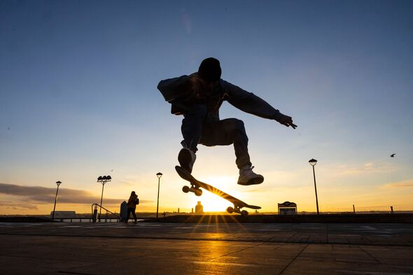 A skateboarder on Liverpool Pier Head performs a trick as the sun sets this evening
