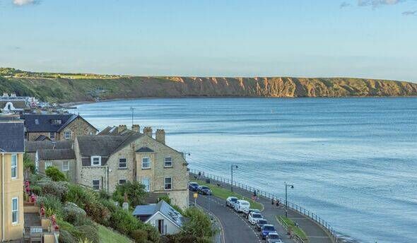 Filey, UK. August 10, 2024. A seaside bay with houses in the foreground and the cliffs of a headland in the distance. A low ev