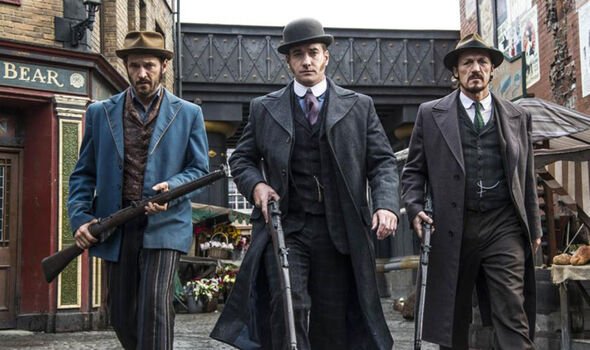 Three men in period clothing hold guns in the street