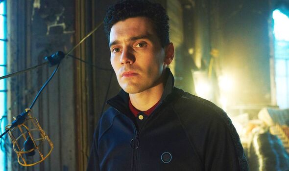 Main in dark jacket stands in delipidated building filled with wires and lights