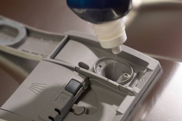 Professional housekeeper carefully measuring and pouring liquid dishwashing detergent into designated dishwasher compartment, pr