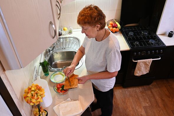 Woman prepares a sandwich in a kitchen with fresh vegetables and fruit on the counter