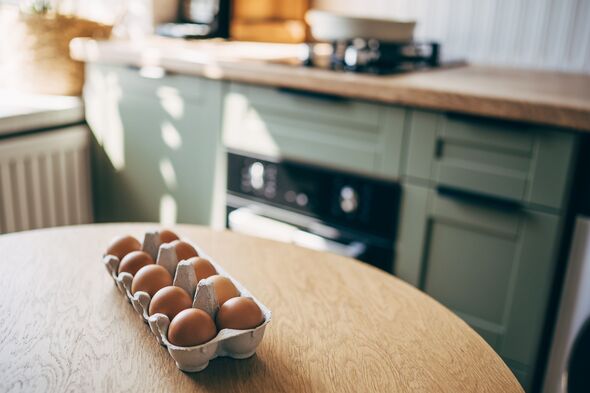A collection of fresh organic brown chicken eggs neatly arranged in a grey recycled paper pulp carton tray placed on a wooden kitchen table with a blu