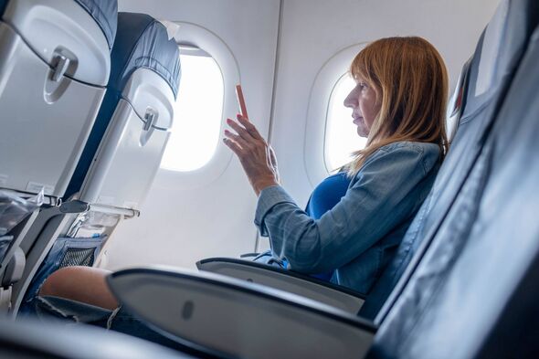 Mature woman traveling by airplane and using mobile phone on flight. Female passenger using smart phone during flight.