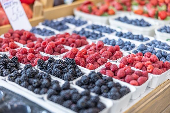 Strawberries, blueberries, blackberries on retail display in farmers market.