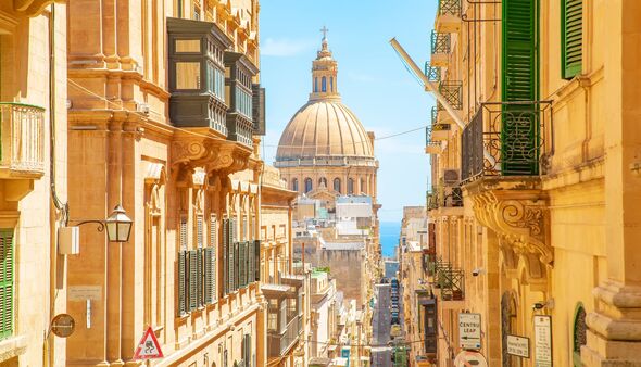 Sunny street in Valletta old town, Malta. Basilica of Our Lady of Mount Carmel on a background.
