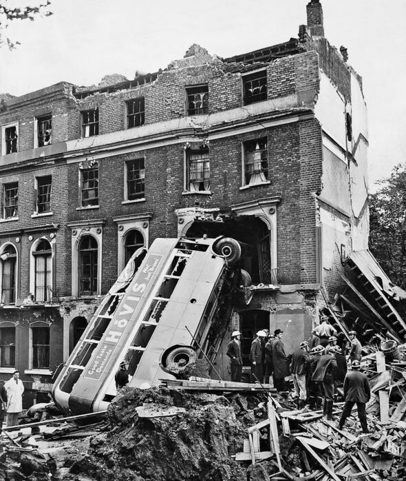 A London double decker bus hit in an air raid leans against a house